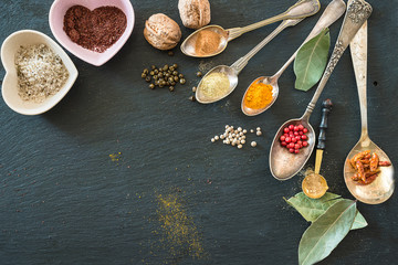 Background with Various of spices in the vintage spoons on the black slate. Copy space, flat lay, selective focus