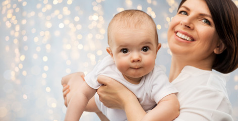 family, child and parenthood concept - happy smiling middle-aged mother holding little baby daughter over festive lights background