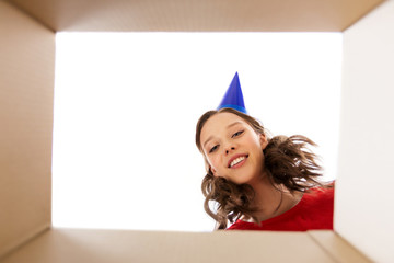 surprise, delivery and holiday concept - happy young woman in birthday party cap looking into open gift box