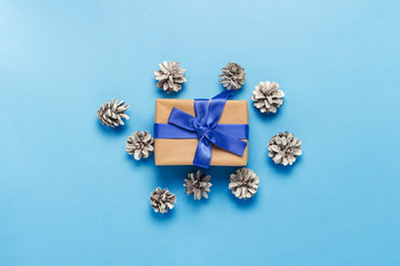 Gift box with blue ribbon and pine cones on a blue background. Minimalism. Flat lay, top view