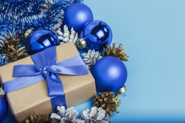 Gift box with blue ribbon, Christmas-tree decorations, balls and white and gold pine cones on a blue background. Concept of Merry Christmas and Happy New Year. Minimalism
