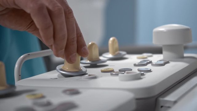 Surgeon operates robotic diagnostic system via remote control panel, hospital, operating roon, hands close-up