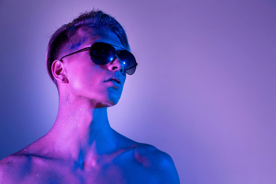Handsome pumped up guy in black sunglasses. Sports guy, attractive male body. Studio shooting with color filters