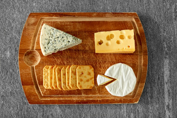 food and eating concept - different kinds of cheese and salty crackers on wooden cutting board