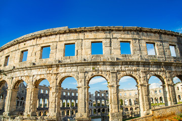Naklejka premium Ancient heritage in Pula, Istria, Croatia. Arches of monumental ancient Roman arena. Detail of historic amphitheater, wide angle view of high walls on blue sky background.