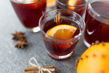 christmas and seasonal drinks concept - glasses of hot mulled wine with orange and cinnamon on grey background