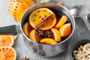 christmas and seasonal drinks concept - pot with hot mulled wine, orange slices and aromatic spices on grey background