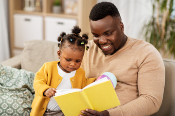family, fatherhood and people concept - happy african american father reading book for baby...