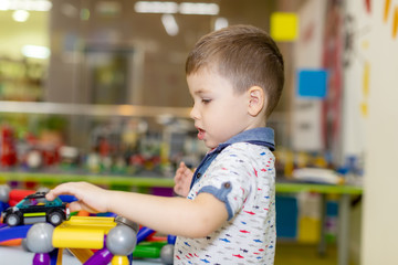 Happy funny little boy child playing with lots of toy cars indoor. Kid boy wearing colorful shirt and having fun at nursery