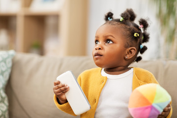 childhood and people concept - little african american baby girl playing with ball and smartphone at home