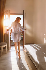 Beautiful young woman standing in doorway at sunset. Back view of sensual lady looking at sunny sky...