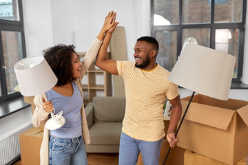 moving, people, repair and real estate concept - happy african american couple with lamps packing...