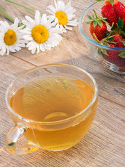 Glass cup of green tea, stawberries with white chamomile flower on wooden background.