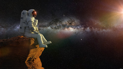 Fototapeta na wymiar astronaut on planet Mars, sitting on a cliff, watching the Milky Way galaxy