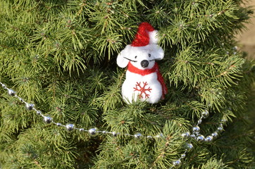 New Year's holidays. On a branch of fresh green spruce sits a decorative white cute little mouse in a red cap.