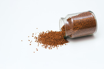 Open glass jar with instant coffee spilled out. White solid background.