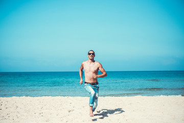 young muscular man resting and posing on the beach. Run towards us