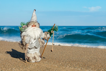 Santa figurine on the beach, tropical ocean background, Christmas travel concept, copy space