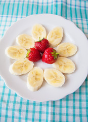 banana and strawberries on white plate and a colorful napkin