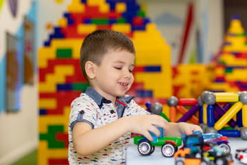 Happy funny little boy child playing with lots of toy cars indoor. Kid boy wearing colorful shirt and having fun at nursery