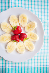 banana and strawberries on white plate and a colorful napkin
