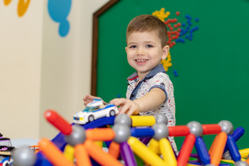 Happy funny little boy child playing with lots of toy cars indoor. Kid boy wearing colorful shirt and having fun at nursery