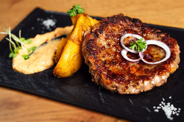 Grilled meat cutlets for burger on dark slate stone board.