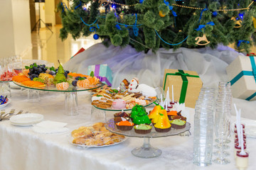 Various fruits, desserts, pastries on the holiday table. New year or Christmas. Decorated Christmas tree.