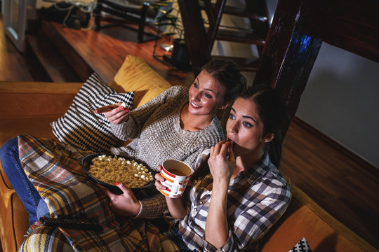 Two female best friends sitting at home on pleasant evening and watching a television show.