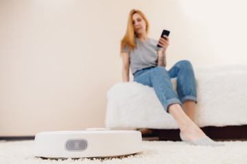 Young girl using automatic smart robot vacuum cleaner working on carpet
