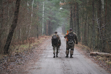 Fototapeta premium rear view, two soldiers with guns walk along a forest road