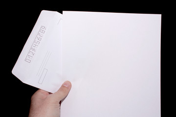 A male hand holds a white blank paper pulled out of a mail envelope. On a black background.