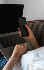 Woman with a laptop is laying on a sofa and using a smartphone. Study and work online, freelance. Self employed girl working with her notebook laying on a couch with a phone.