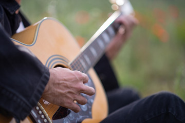 Person playing music with acoustic guitar in the middle of the field, surrounded by green plants and flowers