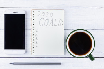 2020 new year goals, plan, action text on notepad on white wooden boards. 2020 goals on blank note paper with copy space for text and smartphone. Cup of coffee over wooden boards