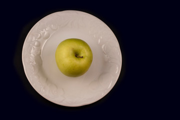 minimalist photography with  golden apple in the center on white plate isolated on black background