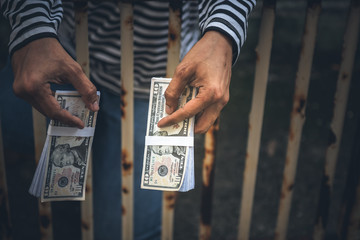 Male criminals Captured in a dirty cage On charges of counterfeiting a bank dollar, in which he held the fake banknote in his hand, to financial crime concept. - obrazy, fototapety, plakaty