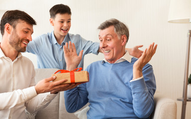 Son And Grandson Congratulating Elderly Man Sitting On Couch Indoor