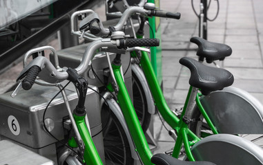 Street transportation green hybrid rent bicycles with electronic form of payment for traveling around the city stand in row on rental network parking lot waiting for cyclists to make bike trip.