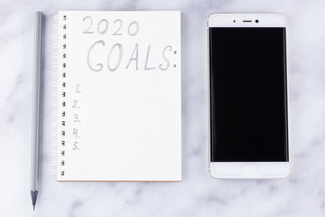 2020 new year goals, plan, action text on notepad on white marble background. 2020 goals on blank note paper with copy space for text and smartphone. Cup of coffee over marble background