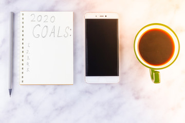 2020 new year goals, plan, action text on notepad on white marble background. 2020 goals on blank note paper with copy space for text and smartphone. Cup of coffee over marble background