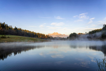 Peaceful mountain scene with calm lake, colorful trees and high peaks in a golden warm light. Scenic view of High Tatras National Park, Slovakia.