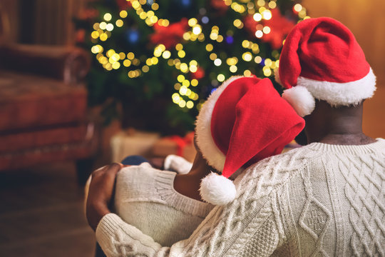 Couple In Santa Hats Cuddling And Looking At Xmas Tree