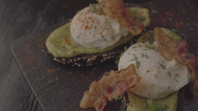 Poached eggs with bacon on toasts. Laid out on black slate.
