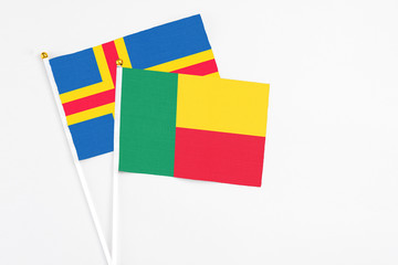 Benin and Aland Islands stick flags on white background. High quality fabric, miniature national flag. Peaceful global concept.White floor for copy space.