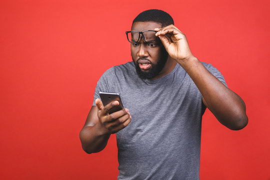 Young african american man using smartphone stressed, shocked with shame and surprise face, angry and frustrated. Fear and upset for mistake. Isolated over red background.