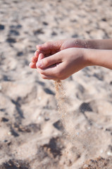 Sand spills out of the hands. On the beach near the sea