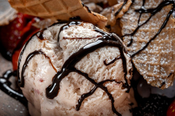 Plate with ice cream and waffles, poured with chocolate topping and decorated with strawberries.