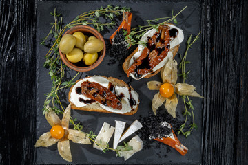 Snacks are laid out on black slate, physalis, salami, cheese and sun-dried tomatoes.