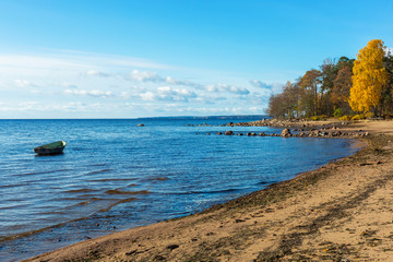 Obraz premium Lonely boat at blue sea. Sandy shore and autumn forest. Northern landscape with a boat on a water surface